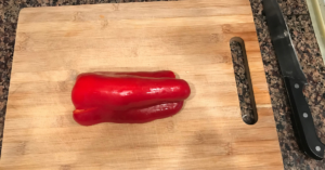 Cutting board with red pepper on it. Knife off to the side.