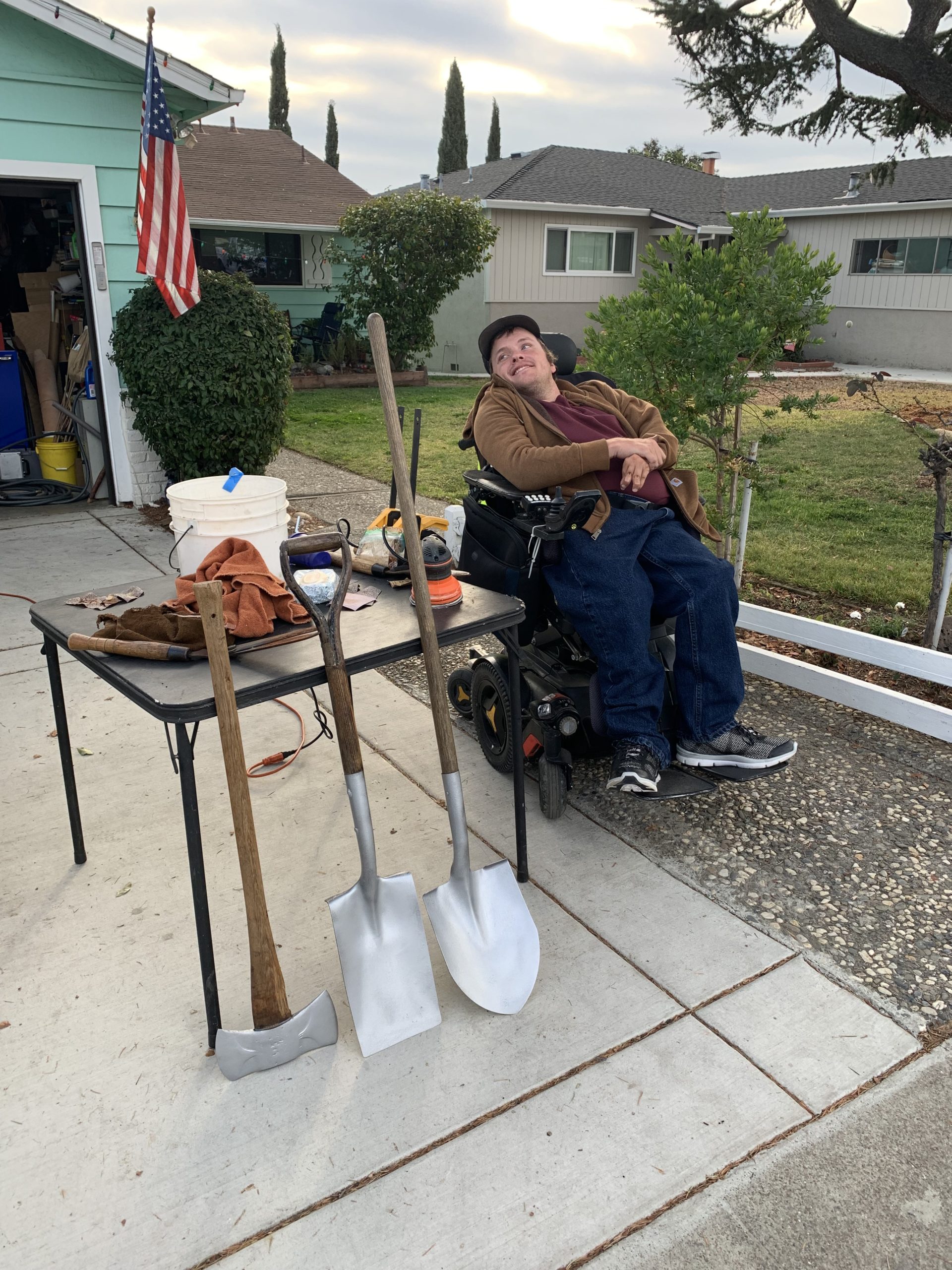 Kyle pictured in the front yard of his family's home. Shovels lean against a table.