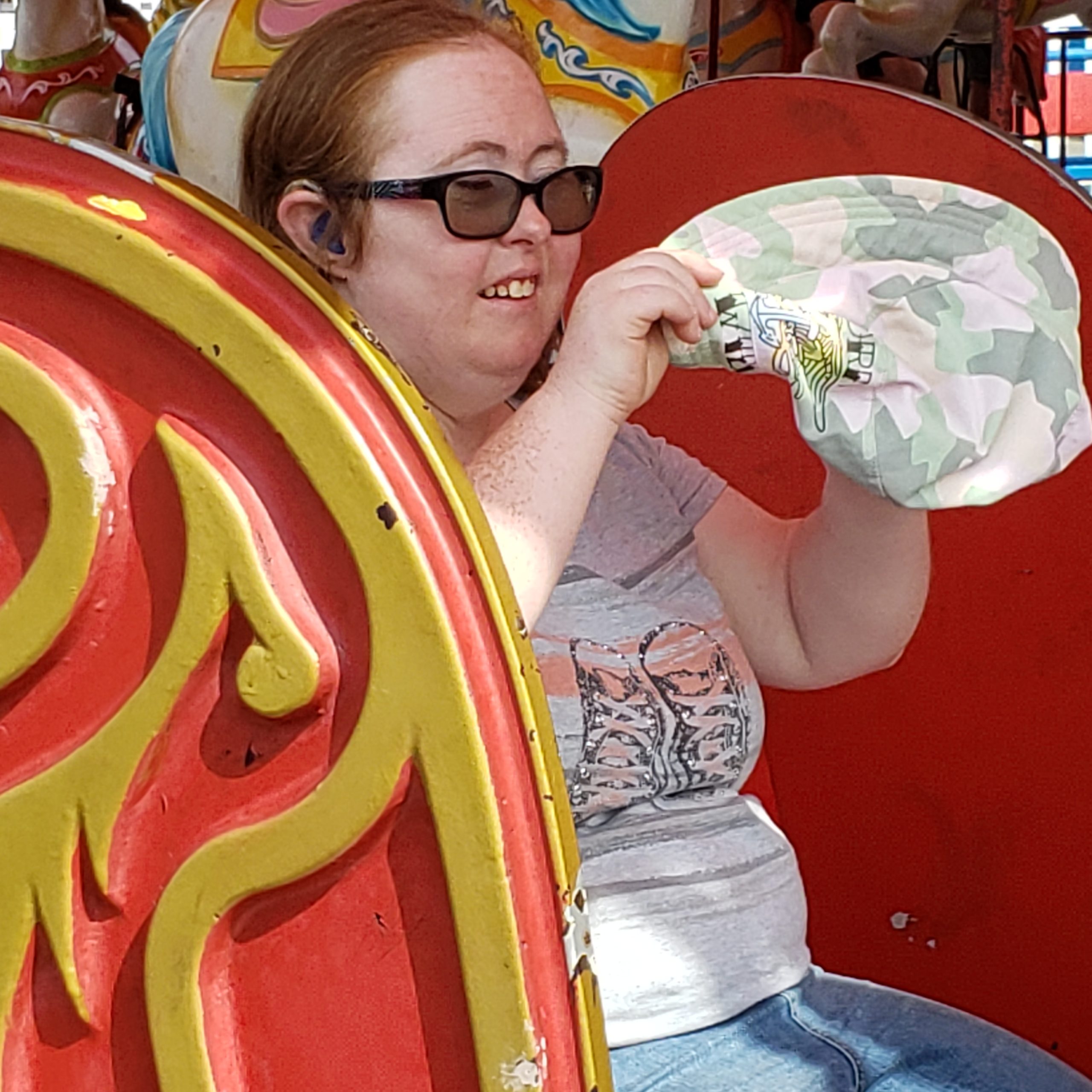 Lauren sitting on an amusement park ride at Coney Island, putting her hat on.