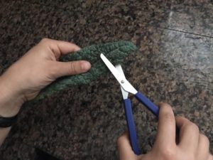 Hands holding a pair of loop scissors, butting a leaf of kale.