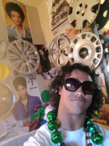 Mikey in his room with hubcaps hanging on his wall. Posters of Bruno Mars and Prince.