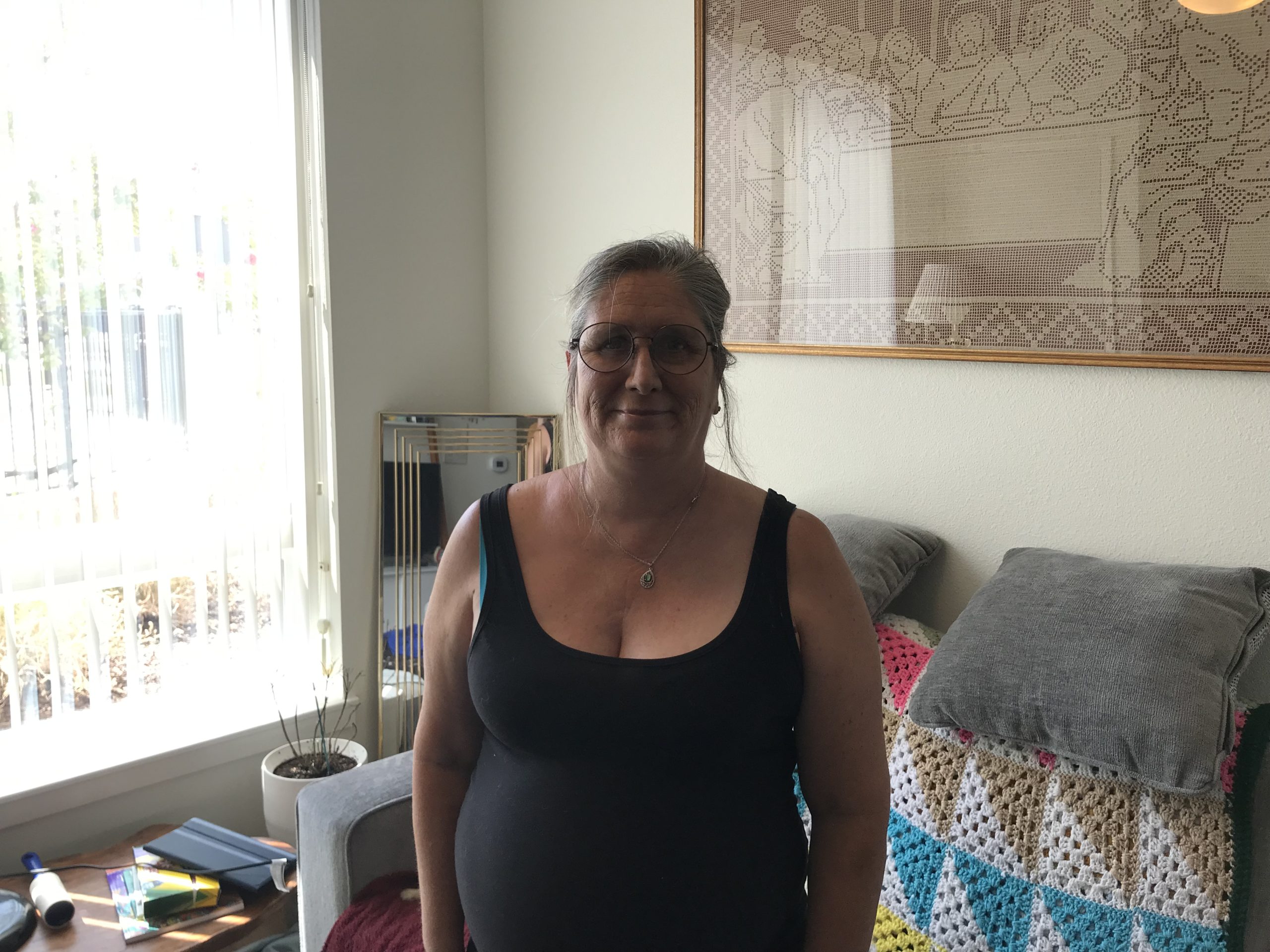 Della smiling and standing in her living room in her apartment.