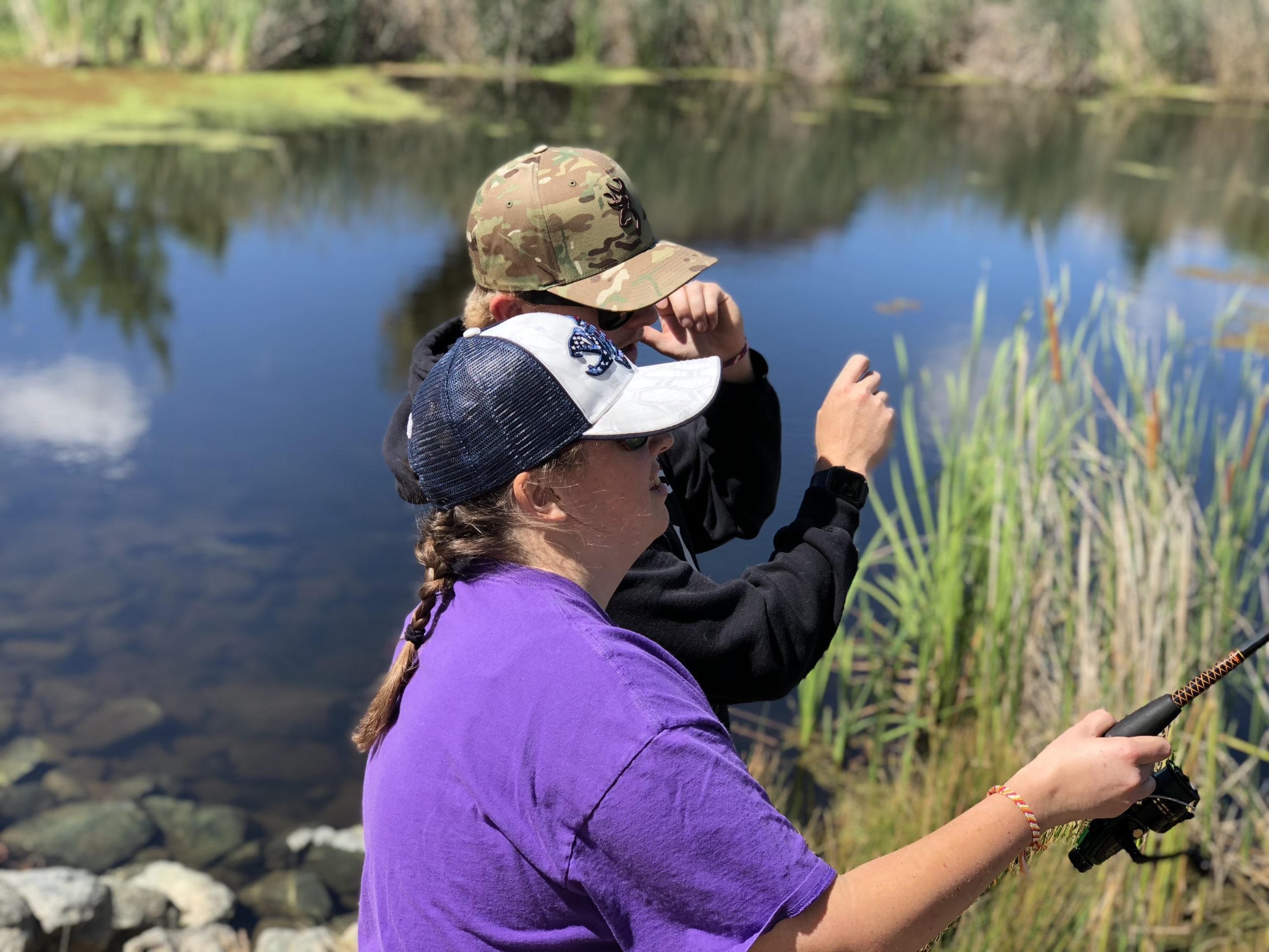 Jennifer with a fishing pole next to a lake, fishing with her brother.
