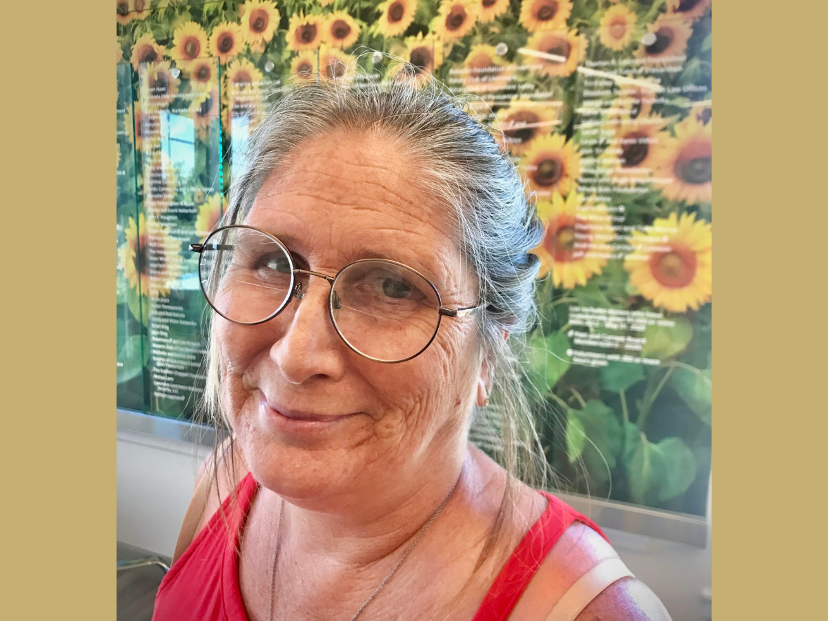 Della smiling in front of picture of sunflowers