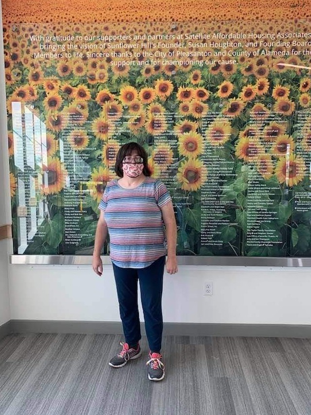 Shannon standing in front of a wall with sunflowers and donor names printed on glass.