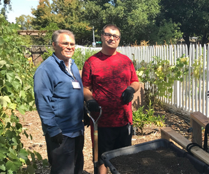 Tim and a program participant standing in the Sunflower Hill Garden next to a wheelbarrow full of dirt.