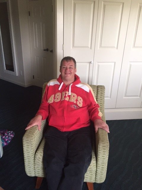 Bruce with 49ers jacket, sitting on chair